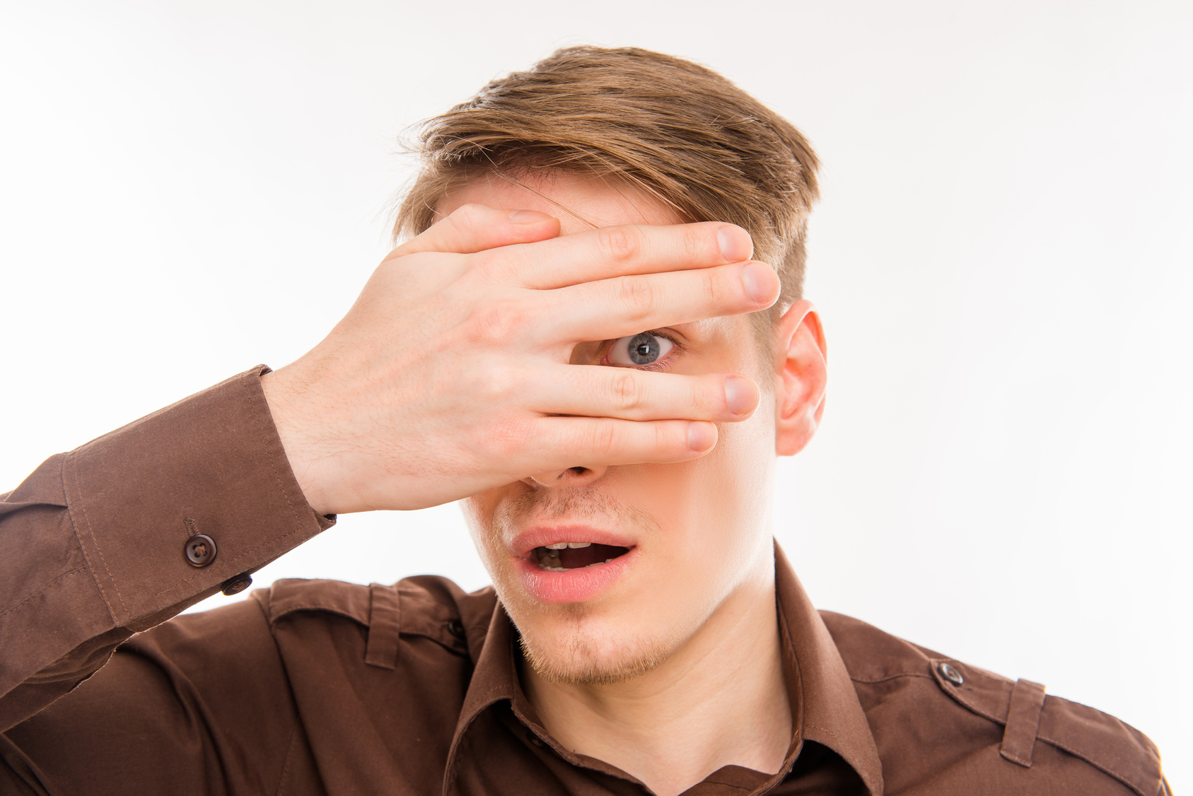 Surprised young man hiding eyes behind his hand