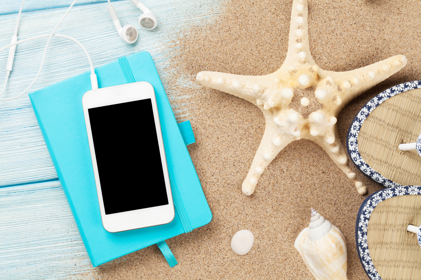 Smartphone and notepad on wooden table with starfish and shells. Top view with copy space